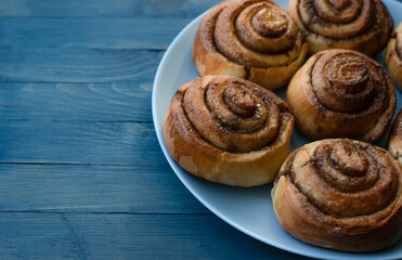 Obraz na płótnie Canvas Homemade swirled rosy buns on a blue plate on the right on a blue wooden background