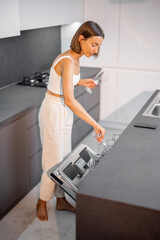 Young housewife is busy, folding glasses into the dishwasher in the kitchen. Daily home routine, comfortable home, new and modern kitchen appliances concept
