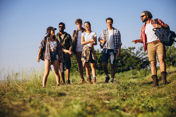 Group of friends, young men and women walking, strolling together during picnic in summer forest, meadow. Lifestyle, friendship,