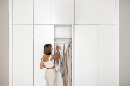 Young woman chooses what to wear, standing near the white closet at home. Concept of choice problem, style and fashion