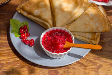 A platter of red currant jam and thin folded pancakes on a plate. Traditional Russian food