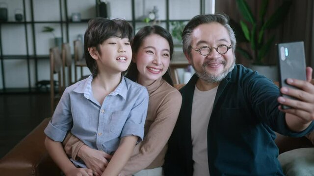 happiness sweet asian family father mother and son sitting together on sofa video calling to grand parent.laugh smiling asian family at home isolation quarantine moment in lockdown state order.