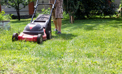 Fototapeta na wymiar mowing grass with a lawnmower in hard-to-reach places on a sunny warm day, horizontal