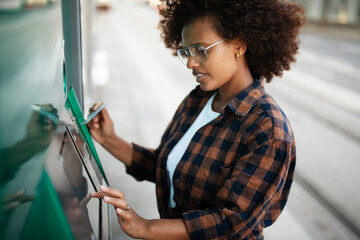 Beautiful african women using ATM machine. Attractive young woman withdrawing money from credit...