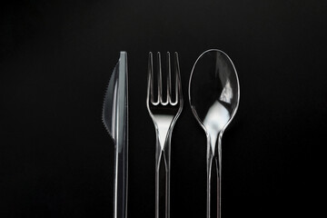 Transparent plastic fork, spoon and knife isolated on black background. 