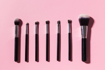 Various make-up brushes on pink background, top view. Cosmetics and beauty concept.