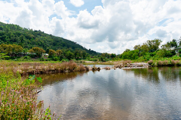 A view of a tourist attraction with a stream flowing behind a mountain sky with beautiful clouds.