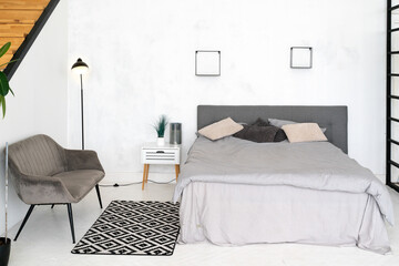 Stylish interior of contemporary room with comfortable bed. Scandinavian design. Room with bed, armchair and black and white rug at the floor