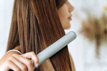Hairdressing. Woman with beautiful long straight hair using hair straightener. Gorgeous girl...