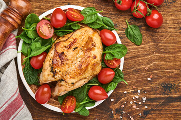 Grilled chicken breast with spinach green salad, pepper and cherry tomatoes in a ceramic plate on an old wooden table background. Top view.
