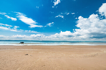 Panorama of a sandy beach, white clouds in a blue sky, a boat on the shore.