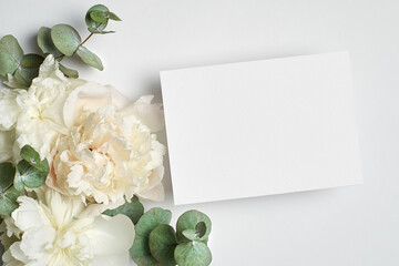Obraz na płótnie Canvas Wedding invitation or greeting card mockup with white peony flowers and eucalyptus twigs