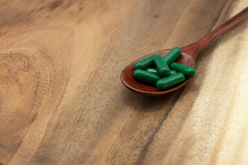 green capsule and a wooden spoon on a wooden background.