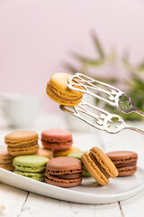 French macarons pastry on coffee table, one held up with pastry tongs