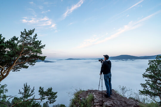 a man photographer in the mountains takes pictures with a camera on a tripod of nature and the morning fog of the hills. the early time is dawn and mist. landscape artist and travel photo. love of