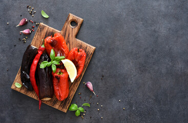 Baked vegetables: eggplant and peppers on a wooden board on a black background.