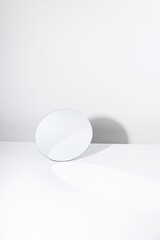 Minimalist mockup of round shaped mirror reflecting white wall placed on white table