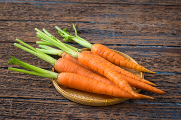 Fresh carrots with small basket on table.