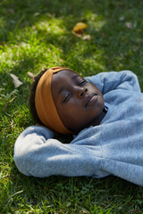 Pretty young black girl lying on grass in grey tracksuit.
