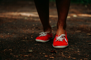 Fototapeta na wymiar Legs in red sneakers on an autumn path in the park. Black leather legs. Sport in summer forest
