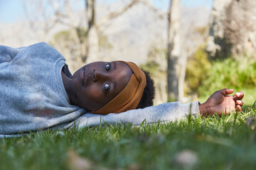Pretty young black girl lying on grass in grey tracksuit.