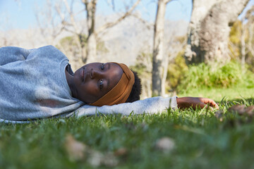 Pretty young black girl lying on grass in grey tracksuit.