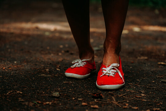 Legs in red sneakers on an autumn path in the park. Black leather legs. Sport in summer forest