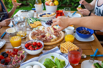 Buffet. The family is sitting at breakfast on the terrace. A large family is eating at the table. The man takes a fig. Jamon, cheeses. Delicious healthy breakfast for a large family. Breakfast at home