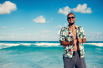 Handsome male in hawaiian shirt smiling against blue sea or the ocean background. Travel vacation holiday. Man enjoy tropical season - obrazy, fototapety, plakaty