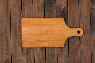 Top view on light brown wooden cutting board on a wooden background