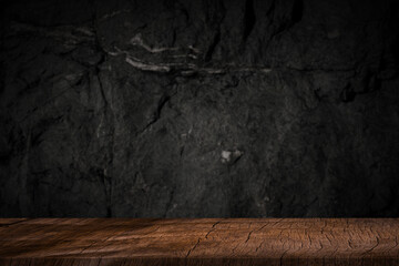 Free space on a wooden table for displaying products with a blurred black wall background.