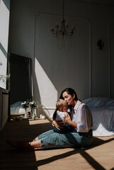 Fototapeta premium happy brunette mom and baby girl kissing on the wooden floor in the rays of light