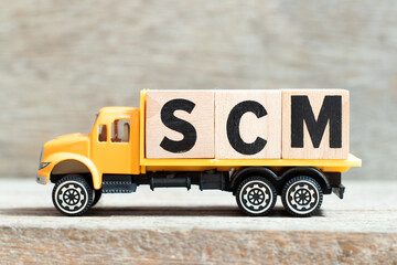 Toy truck hold alphabet letter block in word SCM (Abbreviation of Supply chain management) on wood...