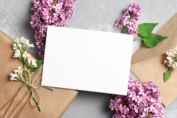 Greeting or invitation card mockup with gift box, envelope and lilac flowers on grey background