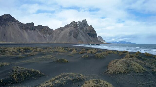 Stokksnes Vestrahorn Drone over black sand beach. in Iceland with jagged mountain peaks by the ocean