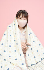 布団を被ってスマホを操作する若い女性