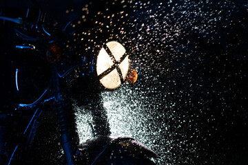 Vintage styled scrambler motorcycle on washing. Splashing water on headlights. Blue illumination at...