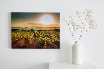 Canvas photo print and flowers in vase, interior decor. Landscape photography hanging on white wall