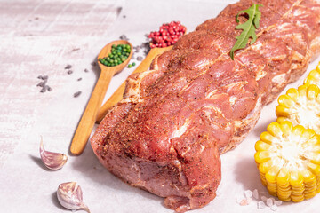 A piece of raw pork loin, marinated fresh meat tied with culinary twine, sweet corn and spices