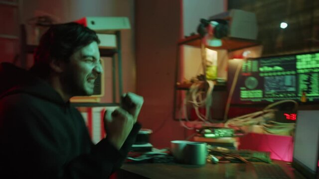 Happy hacker typing on keyboard at night, breaking password, using laptop and bypassing cybersecurity. Young man developing program in dark room. Programmer infecting system with cyber virus