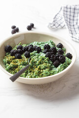 Vegan green oatmeal bowl with matcha tea, spirulina and blackberries. Healthy detox food concept.