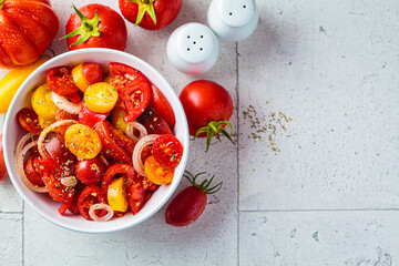 Summer red and yellow tomatoes salad with onions in white bowl.