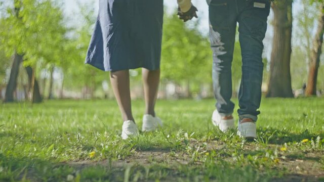 Couple walking in summer park and holding hands, feet close-up, slow motion