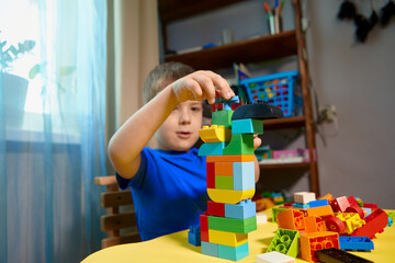 A beautiful boy is playing at home with building blocks. A cute smiling boy is playing with a constructor with a lot of colorful plastic blocks in the room, building a city. Preschool classes.