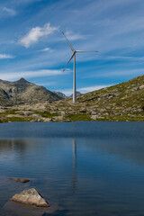 Wind turbine at the top of the Gotthard pass in the Swiss Alps is reflected in the water of the lake