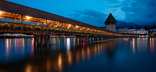 Kapellbrücke, medieval bridge in Luzern at night. The bridge is illuminated, the lights are reflected in the lake