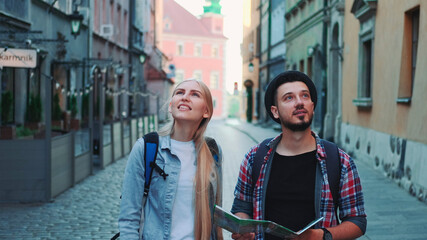 Happy couple of tourists with map walking on central street of old European city. They looking around and smiling.