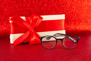 Black eyeglasses on festive red glitter background with a present box