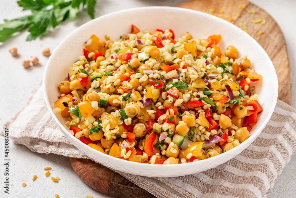 Wall mural Salad of bulgur, chickpeas and vegetables in a bowl close-up. Salad with chickpea, bulgur, tomato, pepper, cucumber, onion, parsley, and lemon juice. Vegan food, Middle Eastern food.