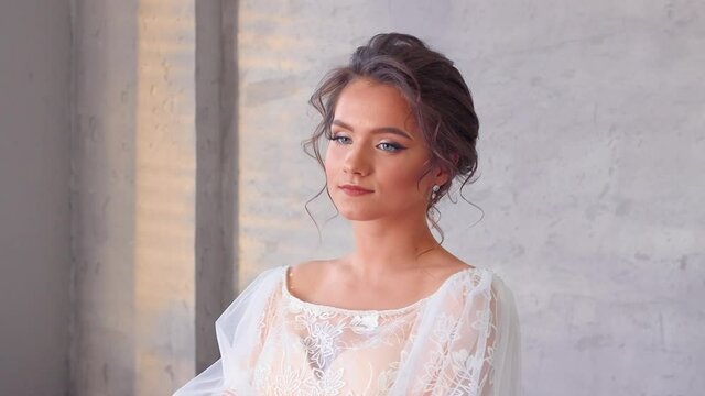 Young pretty model girl posing in a white dress close-up. Gorgeous young woman bride on gray isolated background in studio. There is copy space. UHD 4K.